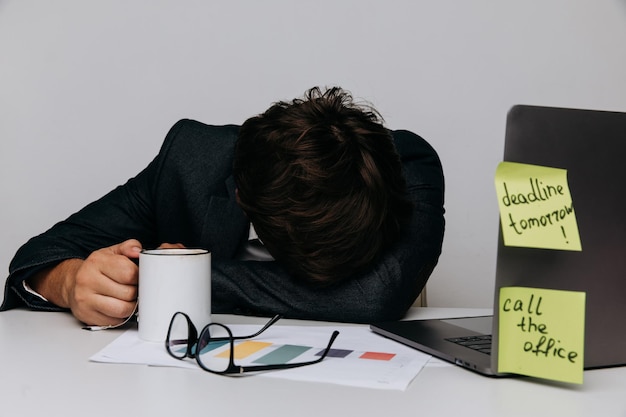 Empresario se acuesta en la oficina con una taza de café Concepto de síndrome de Burnout