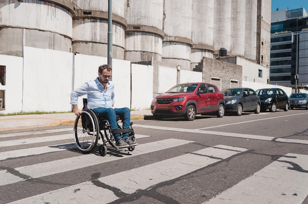 Empresario adulto hispano latino, con barba, gafas y ropa informal, en silla de ruedas cruzando la calle por el paso de peatones yendo al trabajo.