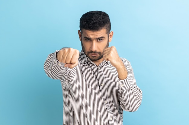 Empresario adulto joven agresivo de pie con puños de boxeo y listo para atacar o defender