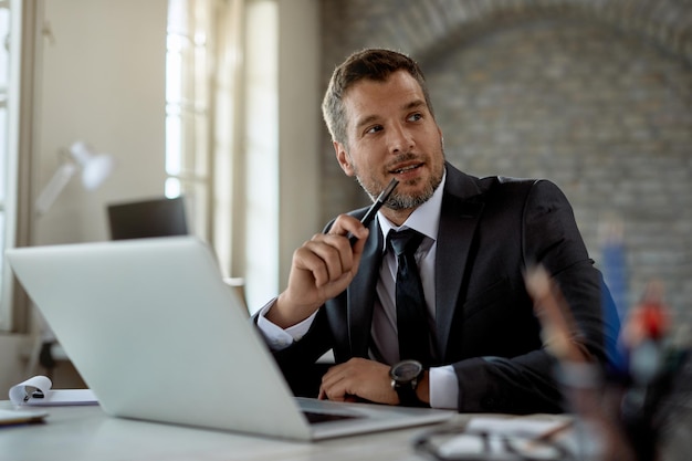 Empresario adulto medio trabajando en una computadora y mirando hacia otro lado en la oficina