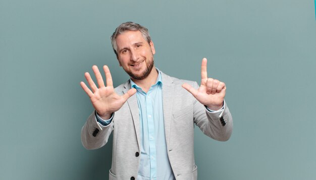 Empresario adulto sonriendo y mirando amigable, mostrando el número siete o séptimo con la mano hacia adelante, contando hacia atrás