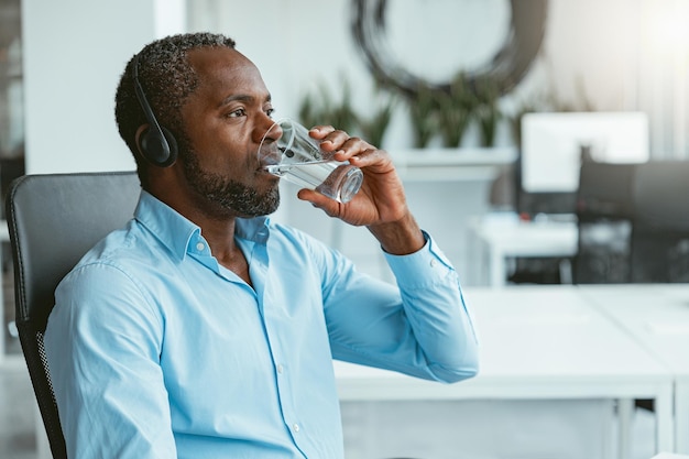 Empresario africano con auriculares bebiendo agua mientras está sentado en el cargo