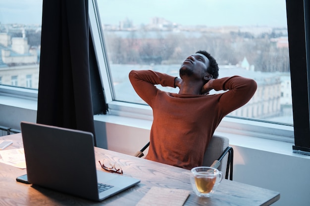 Empresário africano cansado sentado em sua cadeira e descansando depois do trabalho no escritório