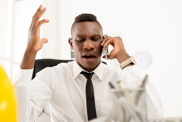 Empresário africano com raiva no escritório usando telefone celular.