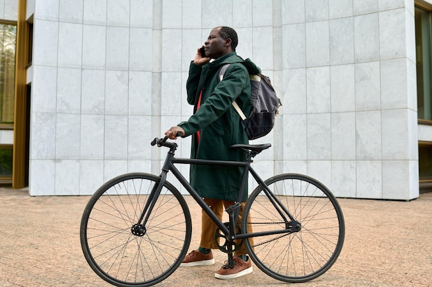 Empresário africano conversando no celular em pé com sua bicicleta ao ar livre