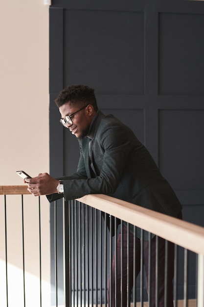 Empresário africano digitando uma mensagem no celular e falando online em pé no escritório