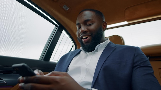 Empresário africano olhando o smartphone para o carro Homem afro segurando o telefone no veículo