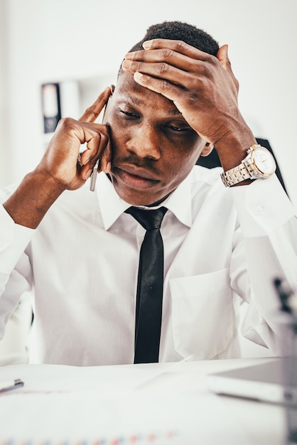 Empresário africano pensativo falando no smartphone no escritório moderno.