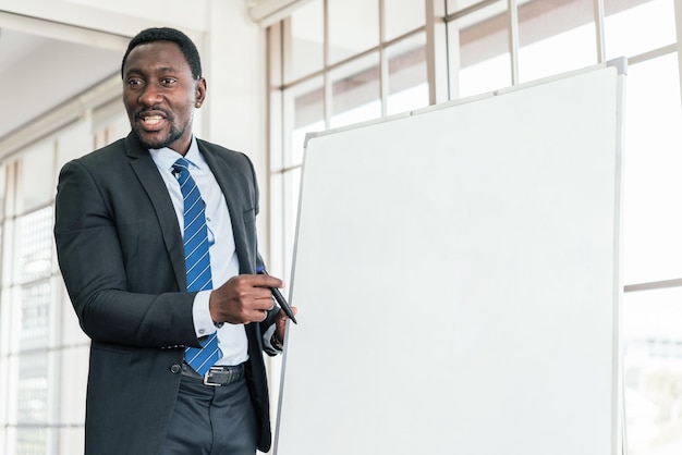 Empresario africano presenta y escucha opiniones en una reunión de negocios con una pizarra vacía