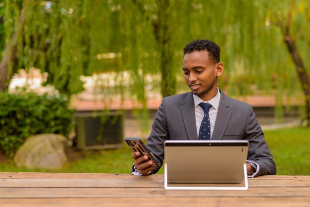 Empresario africano sentado al aire libre con teléfono y computadora portátil