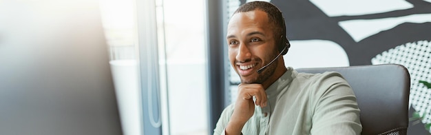 Empresario africano sonriente trabajando en la computadora y tomando notas mientras está sentado en la oficina moderna