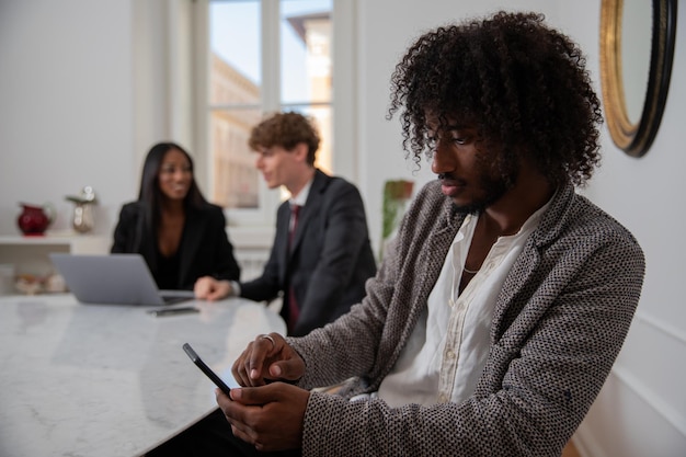 Empresário africano usa seu smartphone no escritório enquanto seus colegas discutem trabalho