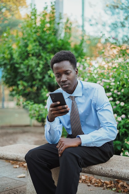 Empresário africano verificando seus e-mails em seu telefone enquanto descansa em um banco