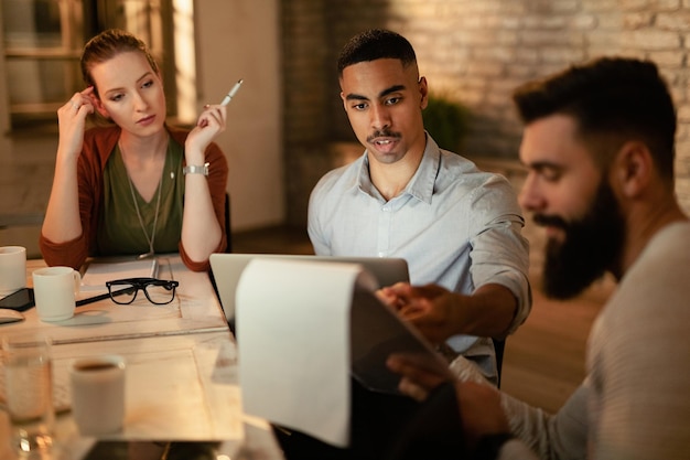 Empresário afro-americano e seus colegas passando por relatórios de negócios em uma reunião no escritório