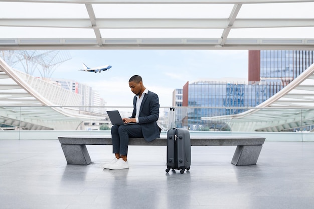 Empresário afro-americano trabalhando no laptop enquanto espera o voo no terminal do aeroporto