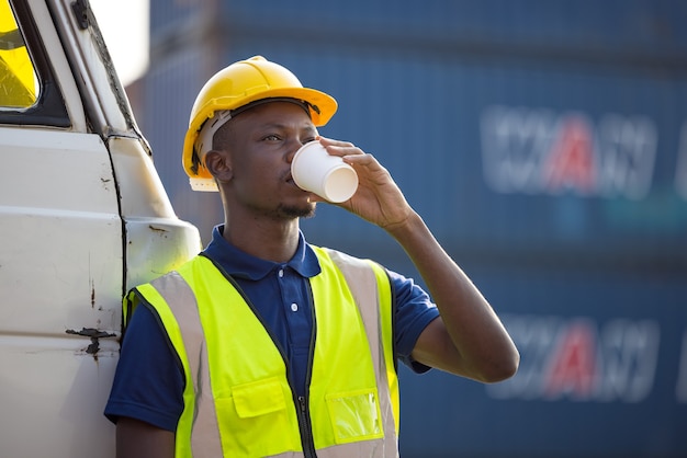 Empresario afroamericano bebiendo café, hombre negro tiene pausa para el café en el lugar de trabajo al aire libre contenedor