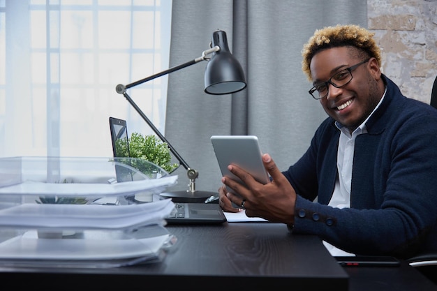 El empresario afroamericano está sentado en una oficina brillante con una computadora portátil y una tableta