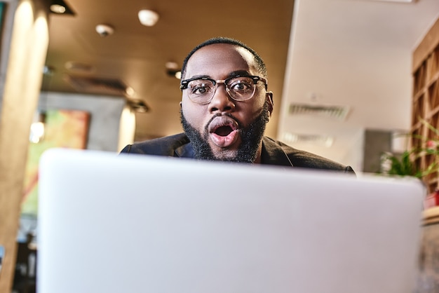 El empresario afroamericano está trabajando con su computadora portátil mientras descansa en el café