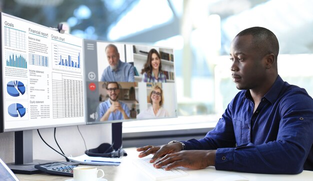 Empresario afroamericano hablando con sus colegas en videoconferencia. Equipo de negocios multiétnico que trabaja desde la oficina con PC, discutiendo el informe financiero de su empresa.