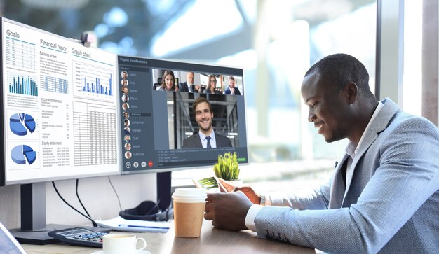 Empresario afroamericano hablando con sus colegas en videoconferencia. Equipo de negocios multiétnico que trabaja desde la oficina con PC, discutiendo el informe financiero de su empresa.