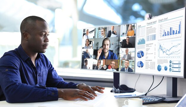 Empresario afroamericano hablando con sus colegas en videoconferencia. Equipo de negocios multiétnico que trabaja desde la oficina con PC, discutiendo el informe financiero de su empresa.