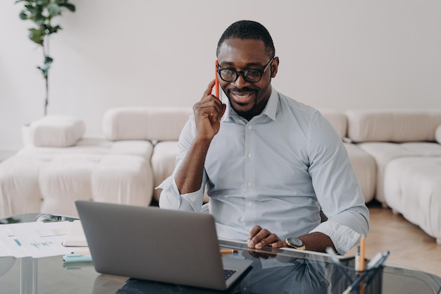 Empresario afroamericano hablando por teléfono en una computadora portátil informa al cliente que vende lleva a cabo negociaciones