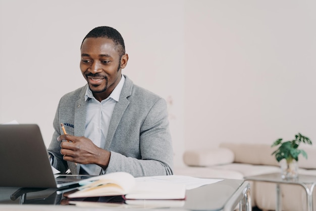 Empresario afroamericano leyendo correo electrónico con buenas noticias en la computadora portátil en el escritorio de la oficina sonriendo