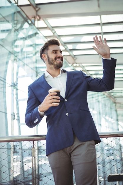 Empresario agitando la mano mientras toma un café en la estación de tren