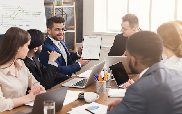 Empresário alegre mostrando gráfico de relatório anual para seus colegas em uma reunião corporativa, torcendo para aumentar o lucro da empresa