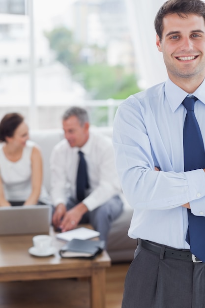 Foto empresario alegre de pie mientras sus colegas están trabajando