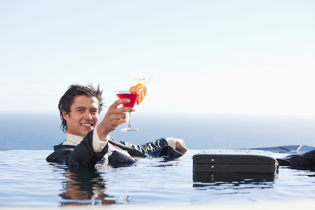 Empresário alegre relaxando em uma piscina com um coquetel
