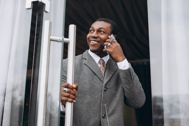 Empresário americano africano em terno cinza clássico, deixando o prédio de escritórios