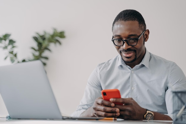 Empresário americano africano segurando telefone usa aplicativos para negócios de comércio eletrônico trabalhando online