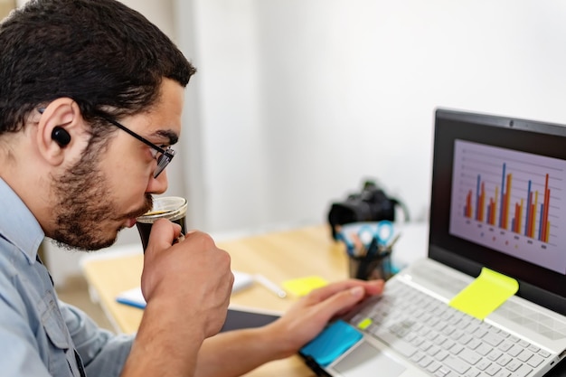 Foto empresário analisando estatísticas no laptop enquanto bebia café no escritório