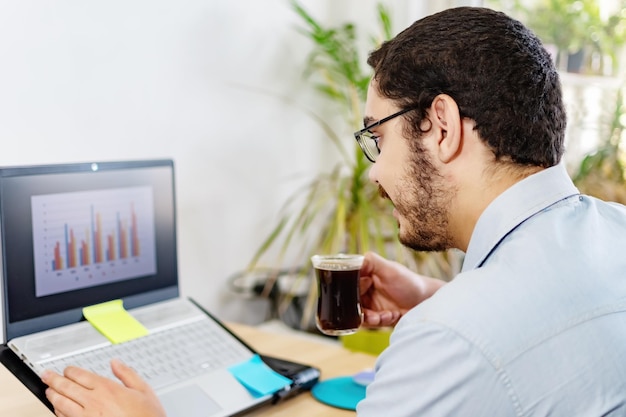 Empresário analisando estatísticas no laptop enquanto toma café no escritório