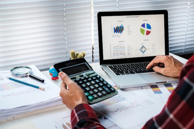 Empresário analisando gráficos de investimento com laptop e calculadora na mesa da mesa de escritório.