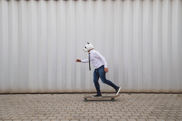 Empresário andando de skate em longboard com uma máscara de urso panda contra uma parede cinza