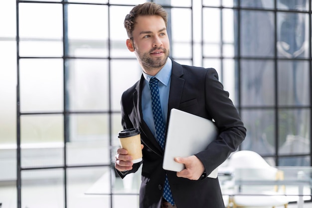 Empresário andando no corredor do escritório com café para viagem