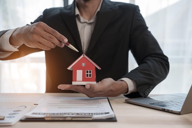 Empresário aprovador de crédito em terno masculino e maquete de modelo de brinquedo de casa Conceito de aprovação de hipoteca de empréstimo à habitação Depois de assinar o contrato