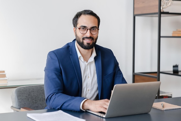 Empresario árabe maduro asesor financiero independiente que trabaja en línea en una computadora portátil en la oficina de forma remota gerente masculino seguro haciendo papeleo aprendizaje electrónico concepto de ocupación