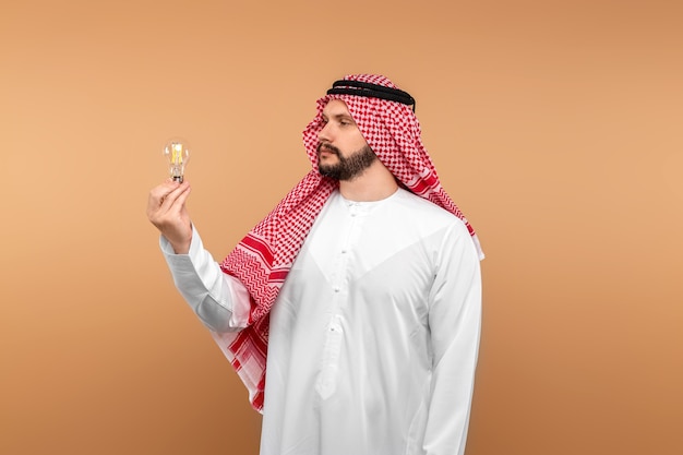 Empresário árabe masculino com roupas nacionais tem uma lâmpada incandescente nas mãos.