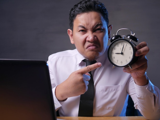 Empresário asiático apontando para o relógio com expressão de raiva