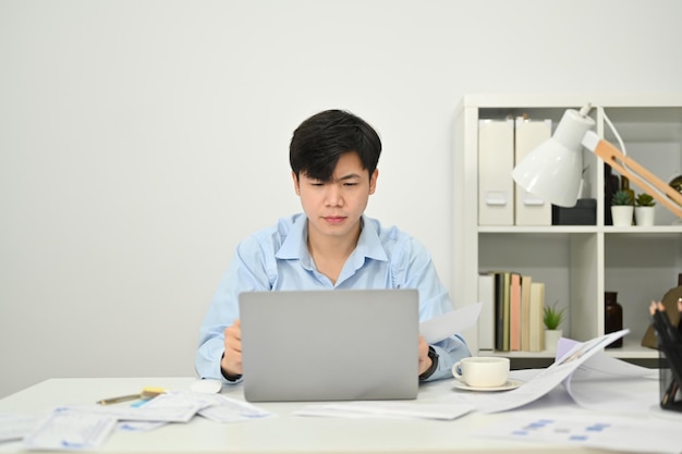 Empresario asiático concentrado revisando el correo electrónico o el marketing en línea en una computadora portátil en el escritorio de la oficina