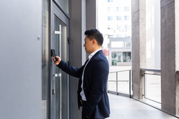 Empresário asiático de sucesso abre a porta do centro de escritório usando um smartphone e um aplicativo NFC