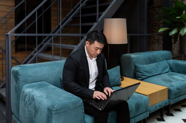 Empresário asiático de sucesso em um terno preto trabalhando em um laptop relaxando em um restaurante