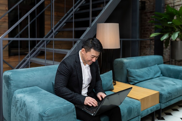 Empresário asiático de sucesso em um terno preto trabalhando em um laptop relaxando em um restaurante