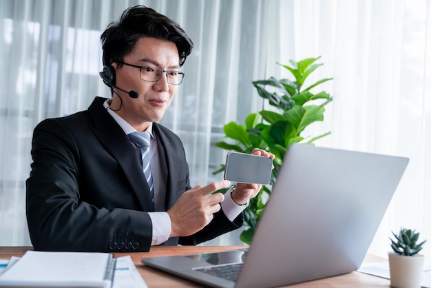 Empresário asiático de televendas trabalha no escritório usando fone de ouvido Jubilant