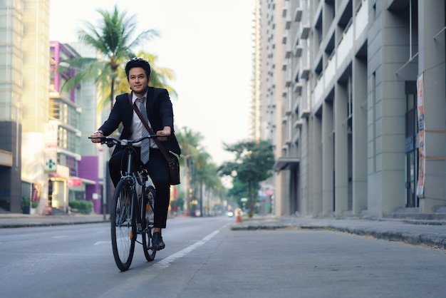 Empresário asiático de terno está andando de bicicleta nas ruas da cidade para seu trajeto matinal para o trabalho. Conceito de transporte ecológico.