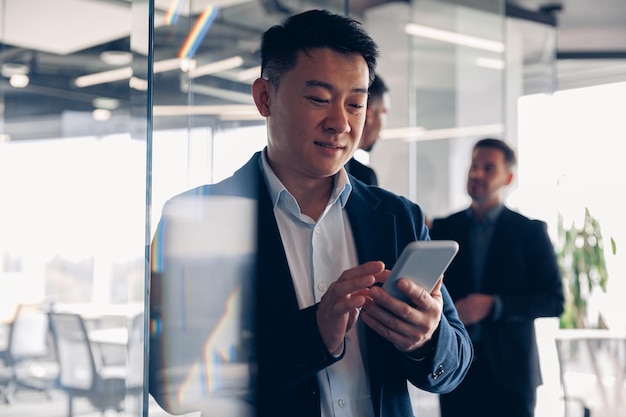 Empresário asiático está usando telefone durante o intervalo no escritório moderno