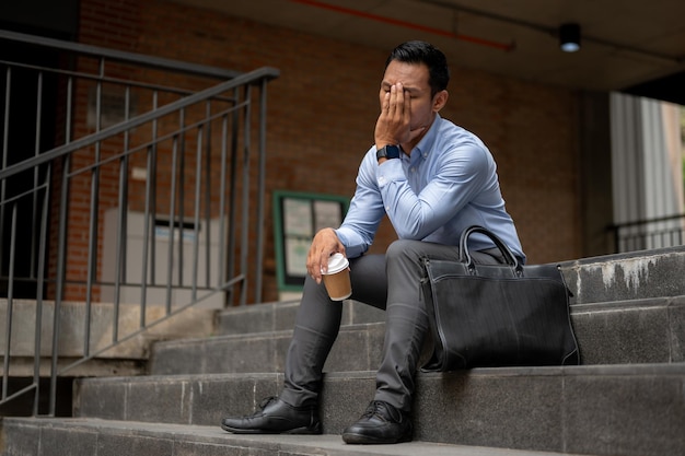 Un empresario asiático estresado que parece cansado e infeliz se sienta en las escaleras de un edificio